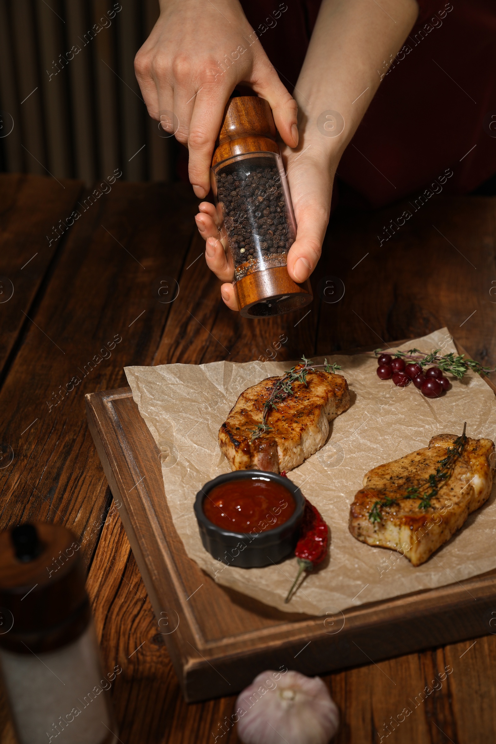 Photo of Food stylist grinding pepper onto meat medallions at wooden table in photo studio, closeup
