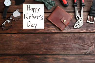 Photo of Greeting card with words HAPPY FATHER'S DAY and male accessories on wooden background, flat lay. Space for text
