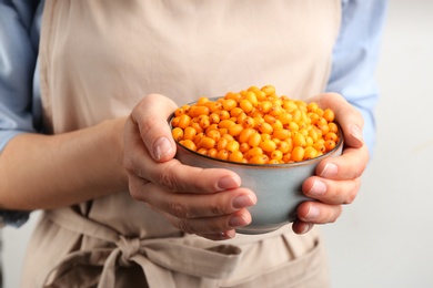 Photo of Woman holding bowl with fresh ripe sea buckthorn on light background, closeup