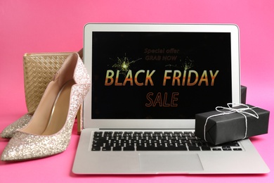 Photo of Laptop with Black Friday announcement, gift and fashionable items on pink background