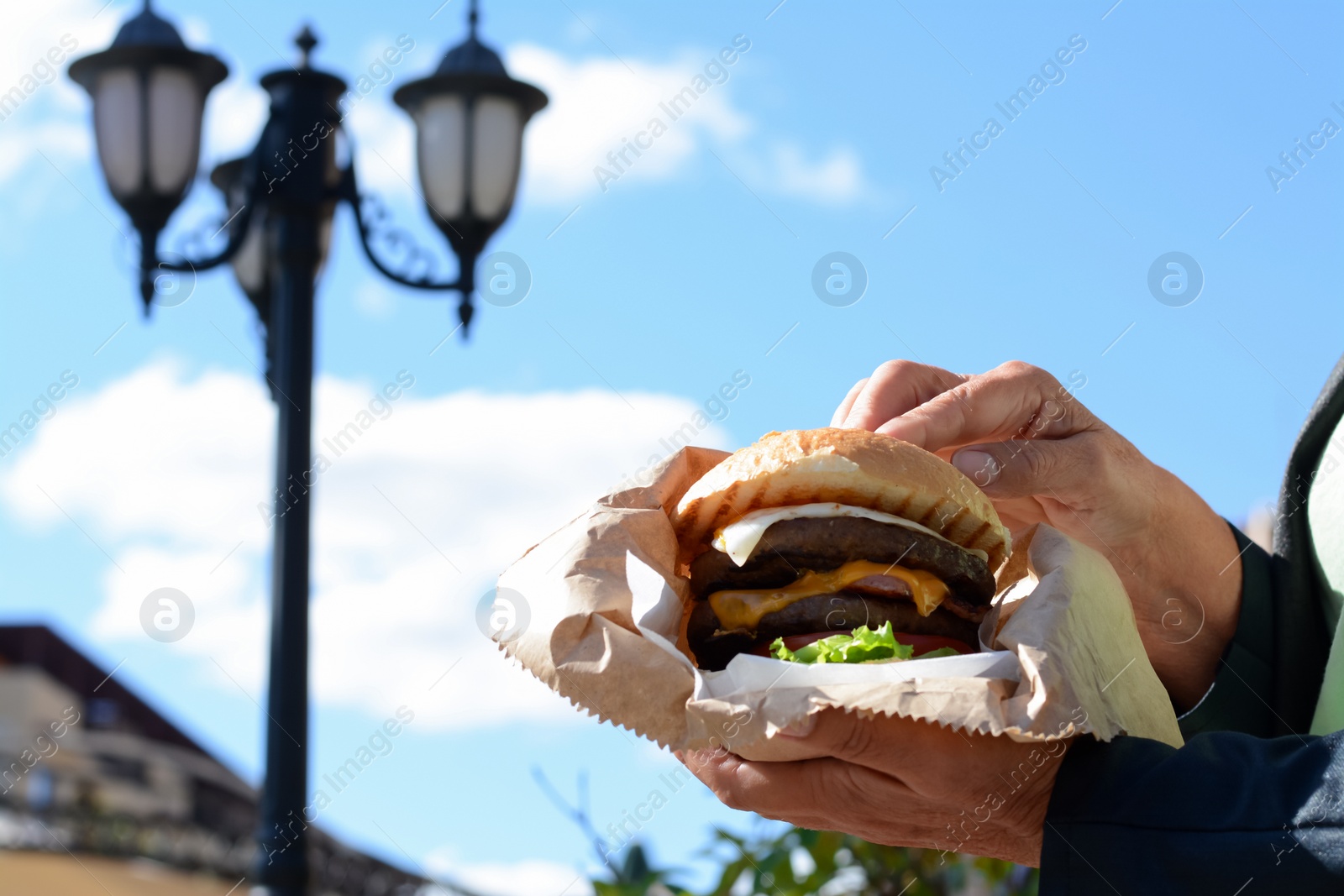 Photo of Woman holding delicious burger in paper wrap on city street, closeup. Space for text