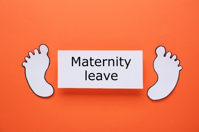 Photo of Note with words Maternity Leave and paper cutout of baby feet on orange background, flat lay