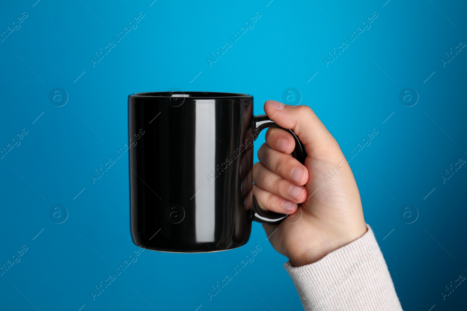 Photo of Woman holding black mug on light blue background, closeup