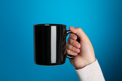 Photo of Woman holding black mug on light blue background, closeup