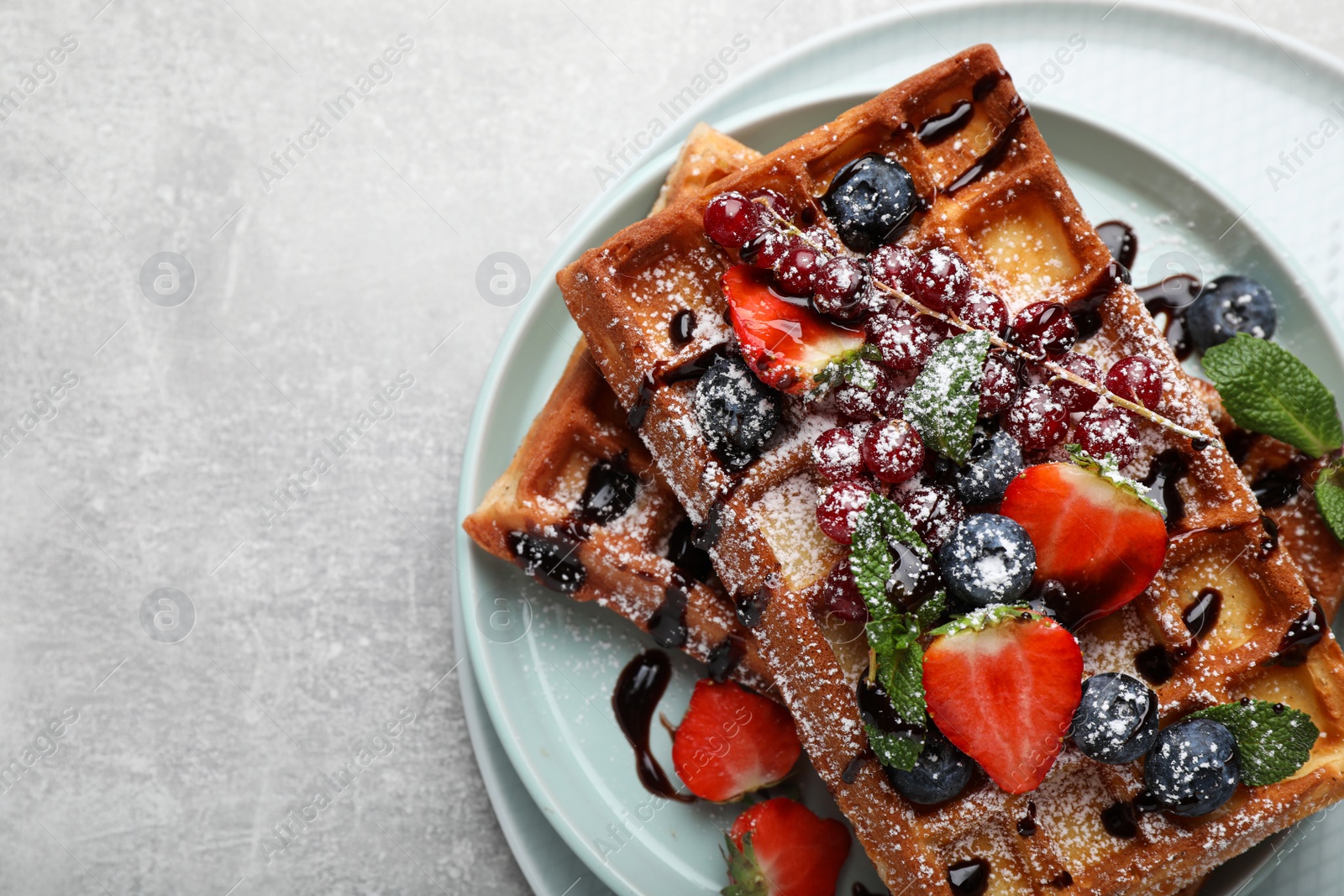 Photo of Delicious Belgian waffles with berries served on light grey table, top view. Space for text