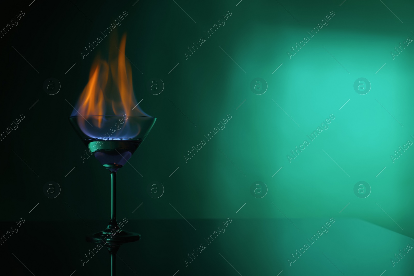 Photo of Cocktail glass with flaming vodka on green background, space for text