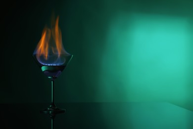 Photo of Cocktail glass with flaming vodka on green background, space for text