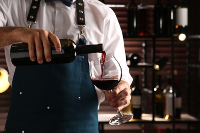 Photo of Bartender pouring red wine into glass indoors, closeup. Space for text