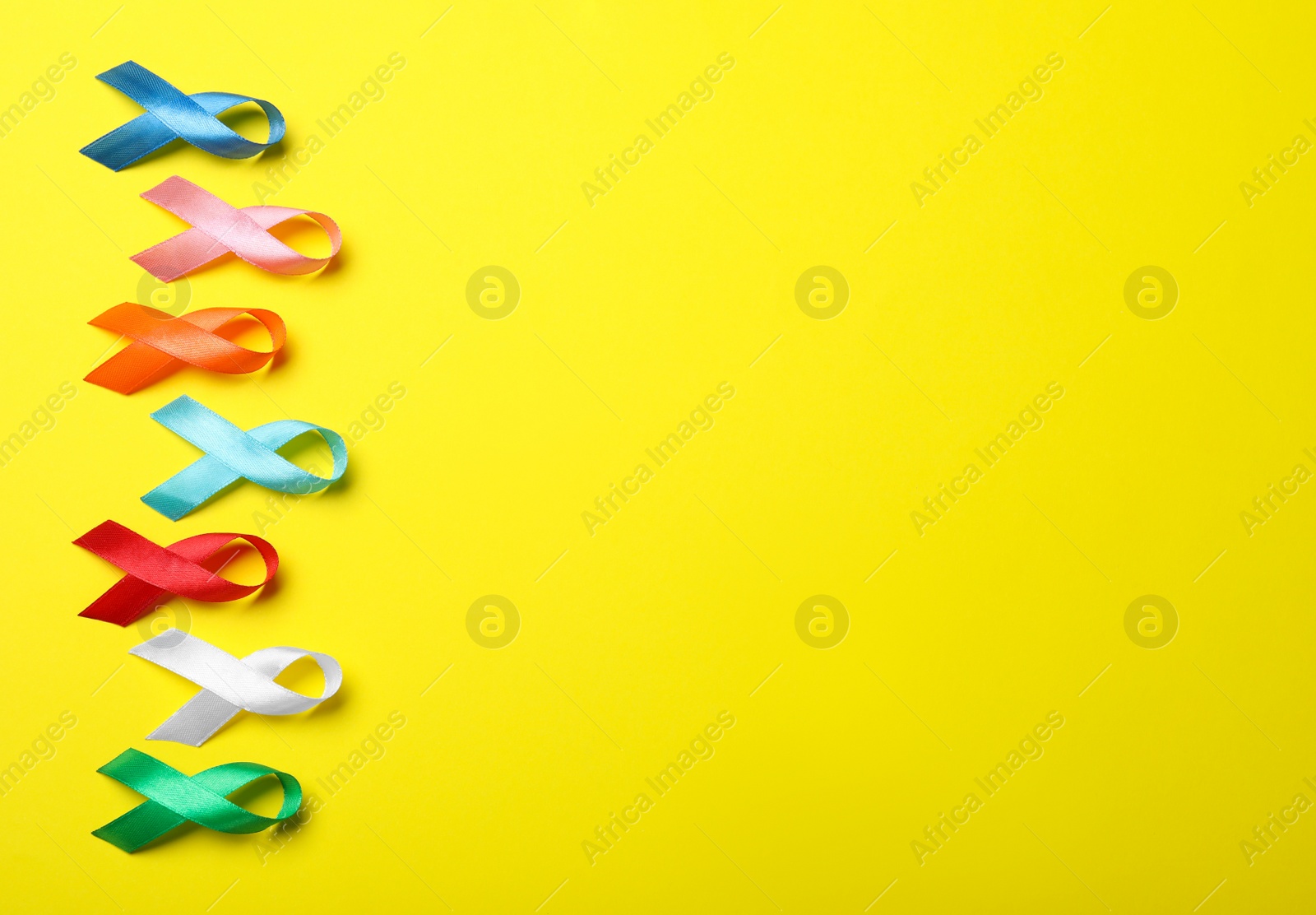 Photo of Colorful ribbons on yellow background, flat lay with space for text. World Cancer Day