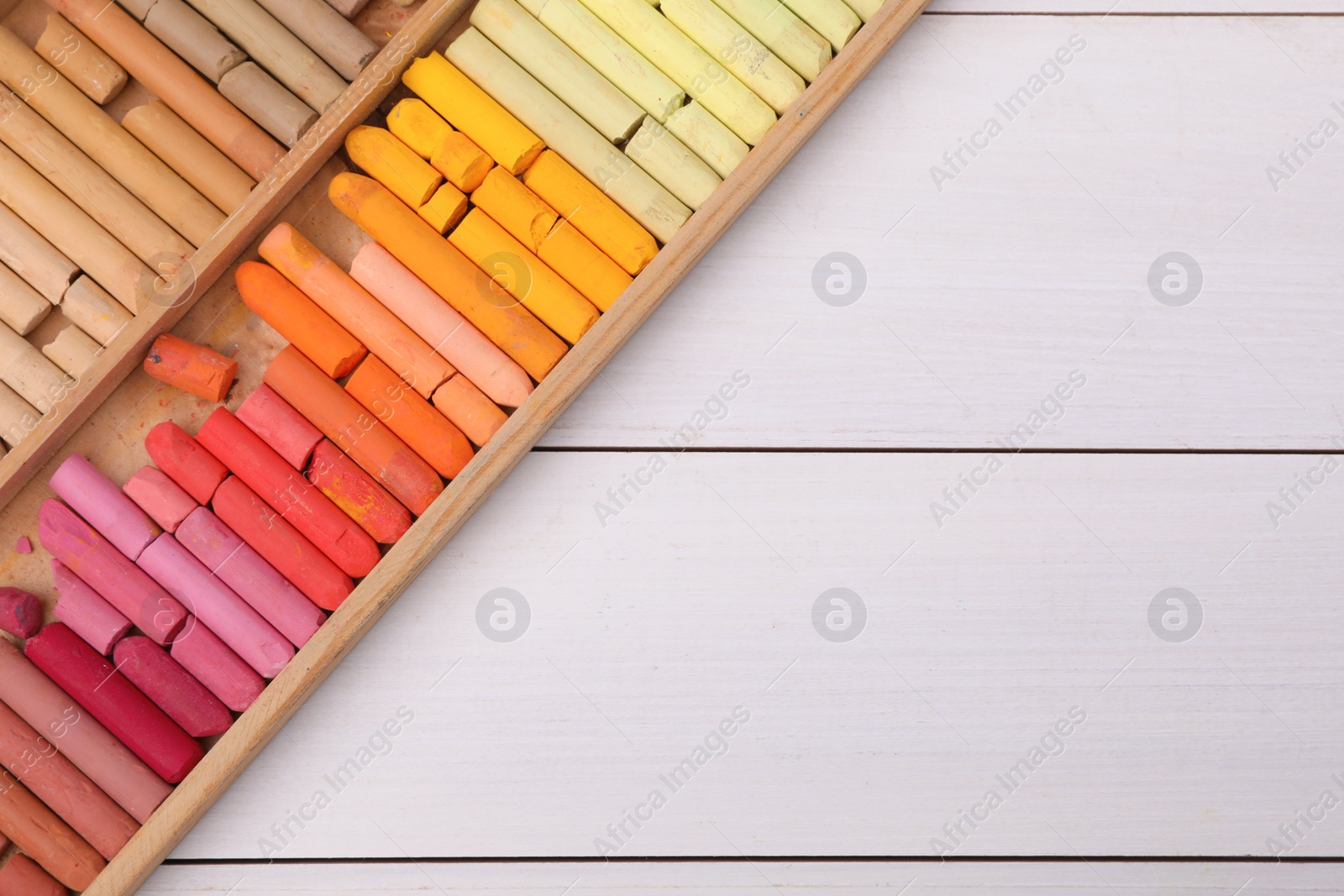 Photo of Set of soft pastels in box on white wooden table, top view with space for text. Drawing material