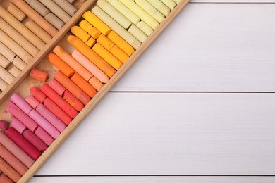 Set of soft pastels in box on white wooden table, top view with space for text. Drawing material