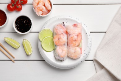 Photo of Delicious spring rolls with shrimps wrapped in rice paper served on white wooden table, flat lay