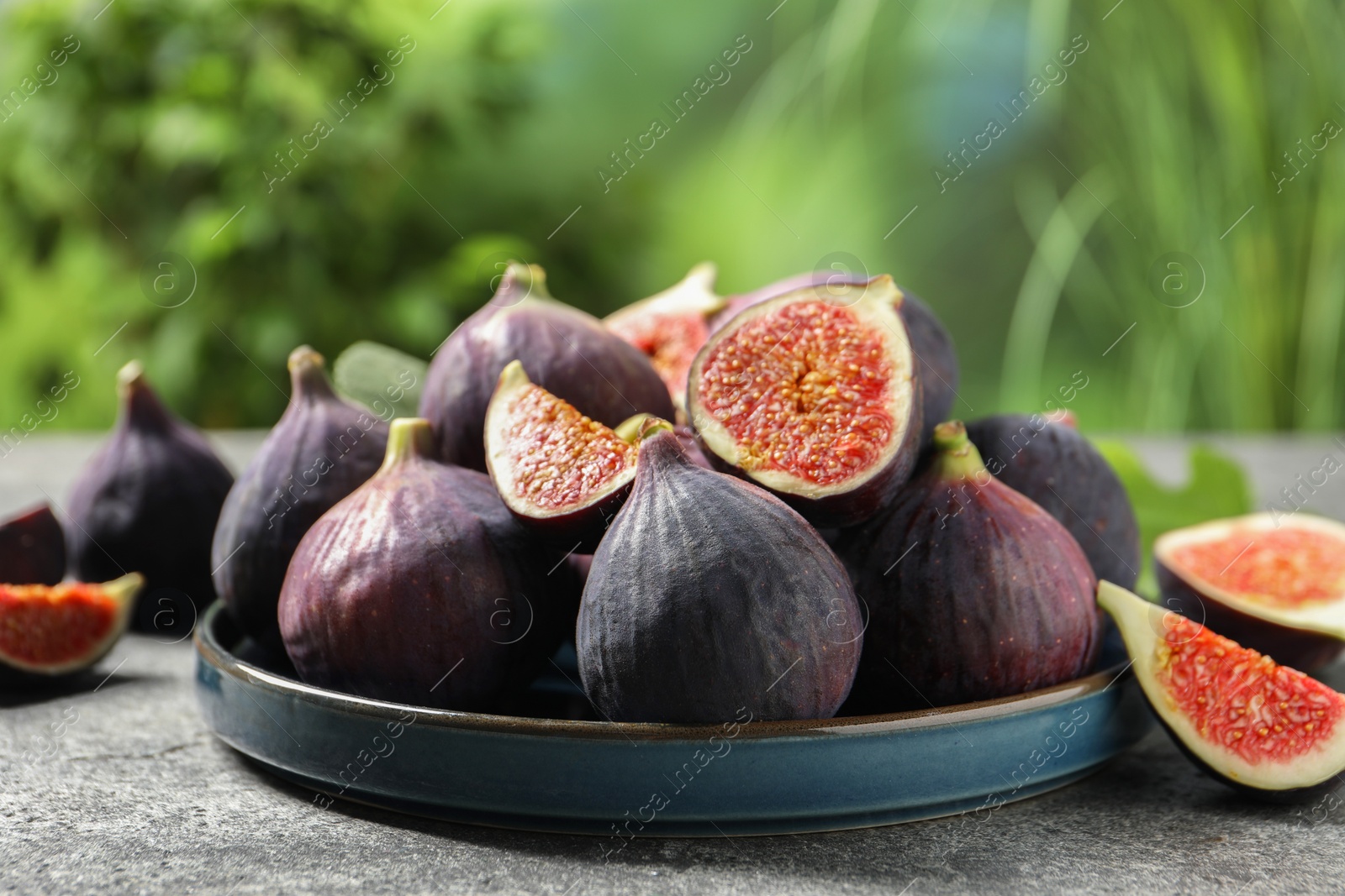 Photo of Whole and cut ripe figs on light grey textured table against blurred green background, closeup
