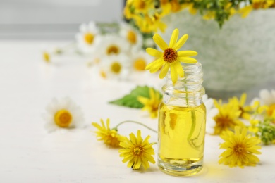 Bottle of essential oil with yellow flowers on table. Space for text