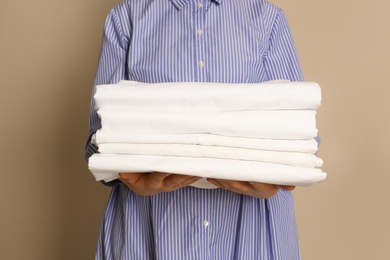 Photo of Woman holding stack of clean bed linens on beige background