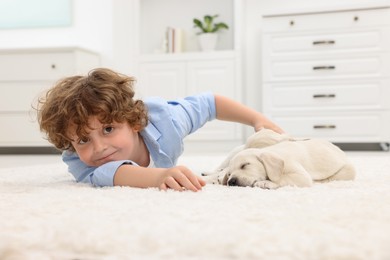 Photo of Little boy lying with cute puppies on white carpet at home