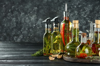 Photo of Cooking oil with different spices and herbs in bottles on grey wooden table. Space for text