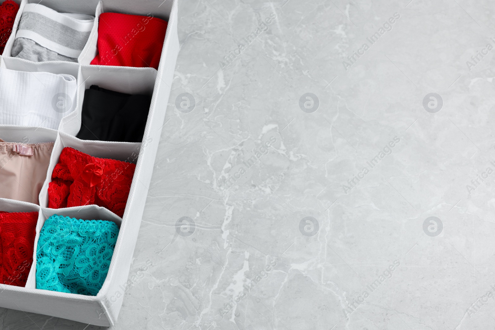 Photo of Organizer with folded women's underwear on light grey marble table, above view. Space for text