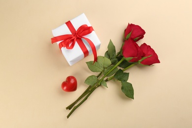 Beautiful gift box, roses and red heart on beige background, flat lay. Valentine's day celebration