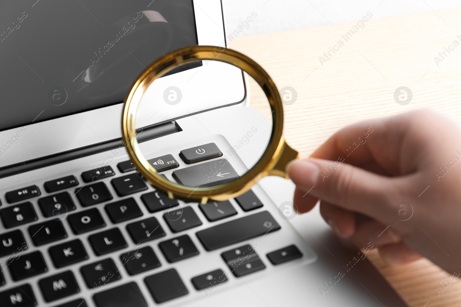 Photo of Woman looking through magnifying glass at laptop on table, closeup. Search concept
