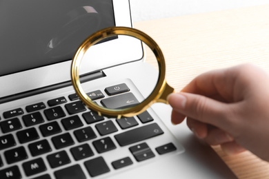 Photo of Woman looking through magnifying glass at laptop on table, closeup. Search concept