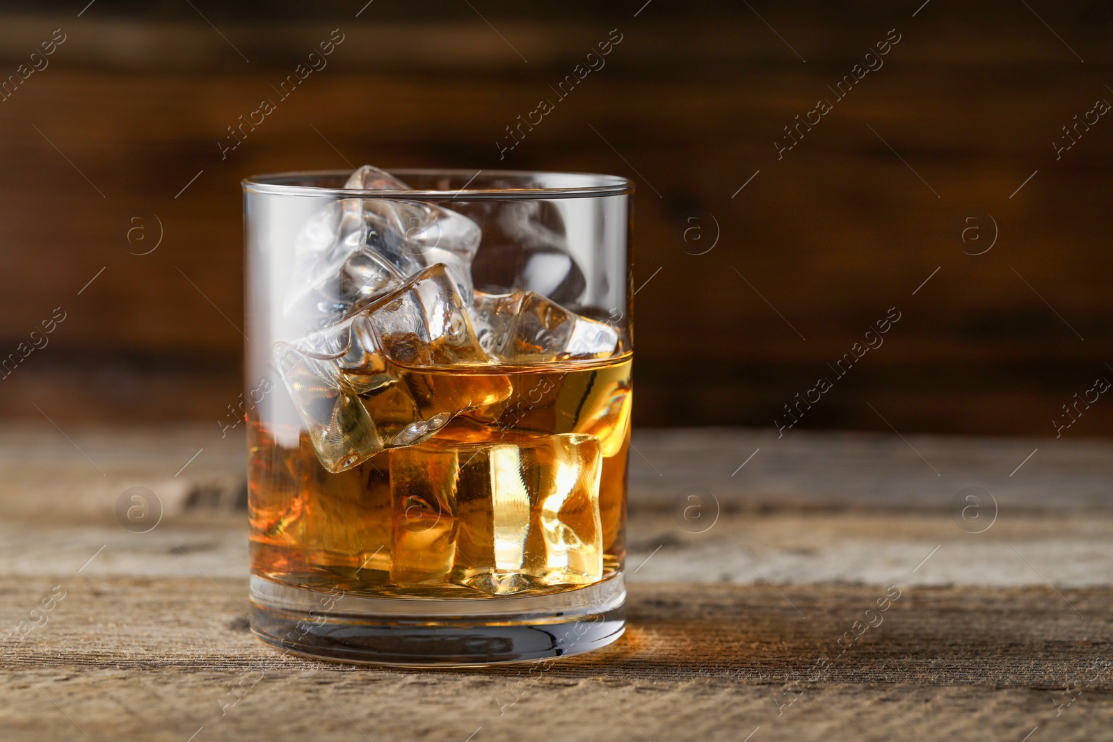 Photo of Whiskey with ice cubes in glass on wooden table, closeup. Space for text