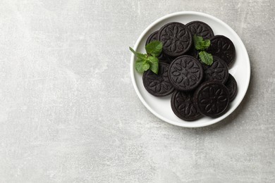 Photo of Plate with tasty sandwich cookies and mint on grey textured table, top view. Space for text