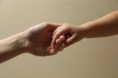 Mother and child holding hands on beige background, closeup