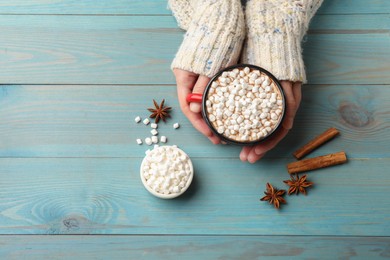 Photo of Woman with cup of tasty hot chocolate and marshmallows at light blue wooden table, top view. Space for text