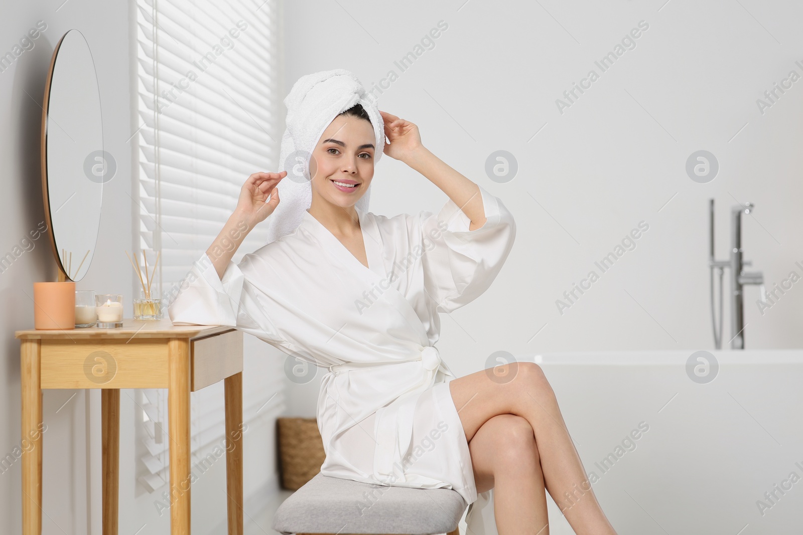 Photo of Beautiful happy woman in stylish bathrobe sitting on bench in bathroom