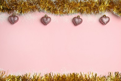 Photo of Shiny golden tinsel, Christmas baubles and snow on pink background, flat lay. Space for text