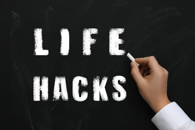 Image of Man writing words Life Hacks with chalk on blackboard, closeup