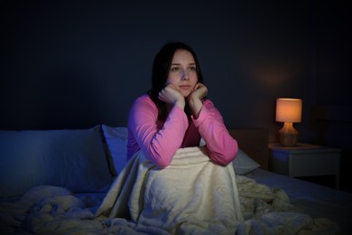 Photo of Young woman watching TV on bed at night