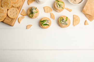 Photo of Delicious crackers with humus and cucumber on white wooden table, flat lay. Space for text