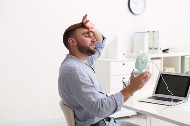 Photo of Man enjoying air flow from fan at workplace