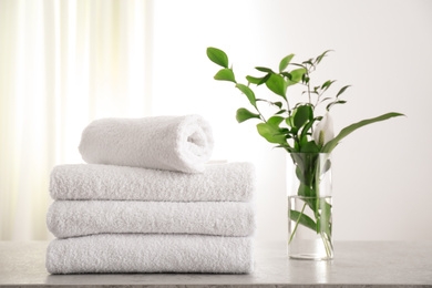 Photo of Fresh towels and green branches on light grey stone table in bathroom