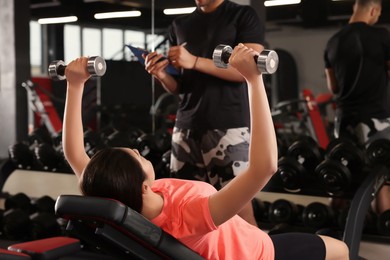Photo of Young woman working out with professional trainer in modern gym
