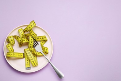 Photo of Measuring tape and fork on violet background, top view with space for text. Weight loss concept