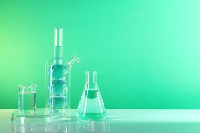 Photo of Laboratory analysis. Different glassware on table against green background, space for text