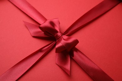 Photo of Bright satin ribbon with bow on red background