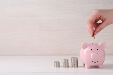 Photo of Financial savings. Woman putting coin into piggy bank at white wooden table, closeup. Space for text