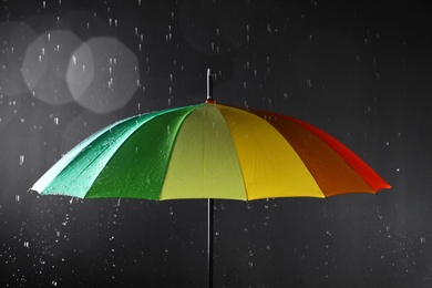 Photo of Bright umbrella under rain on dark background