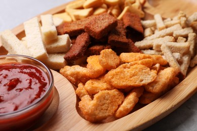 Photo of Wooden tray with different crispy rusks and dip sauce on table, closeup