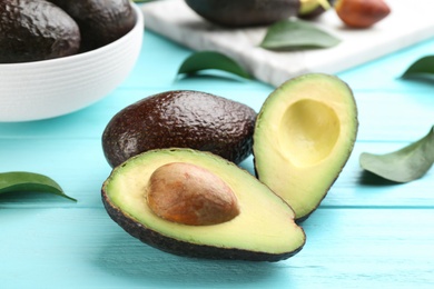 Whole and cut avocados with green leaves on turquoise wooden table, closeup