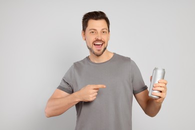 Photo of Happy man holding tin can with beverage on light grey background
