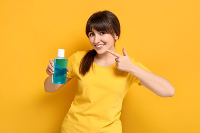 Photo of Young woman with mouthwash pointing at her healthy teeth on yellow background