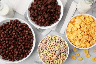 Photo of Different delicious breakfast cereals and milk on white marble table, flat lay