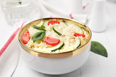 Photo of Tasty couscous with tomatoes, cucumber and basil on white tiled table, closeup