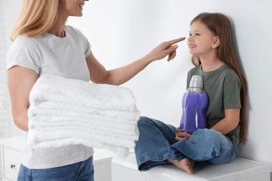 Photo of Mother and daughter holding clean towels and fabric softener in bathroom