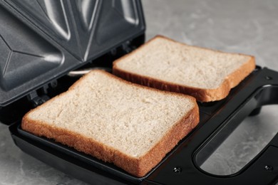 Photo of Modern sandwich maker with bread slices on grey table, closeup